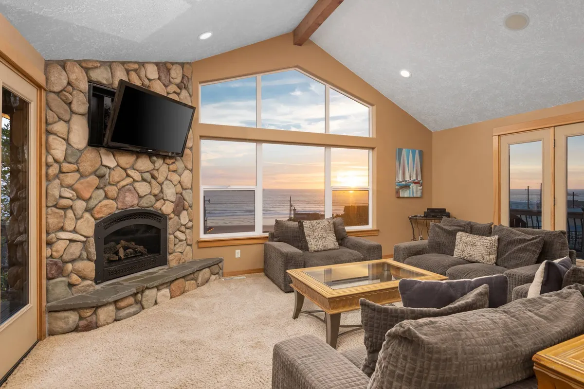 A warm, inviting living space featuring a stone fireplace, large windows with sunset views, and a comfortable seating arrangement perfect for family movie nights or board game sessions.