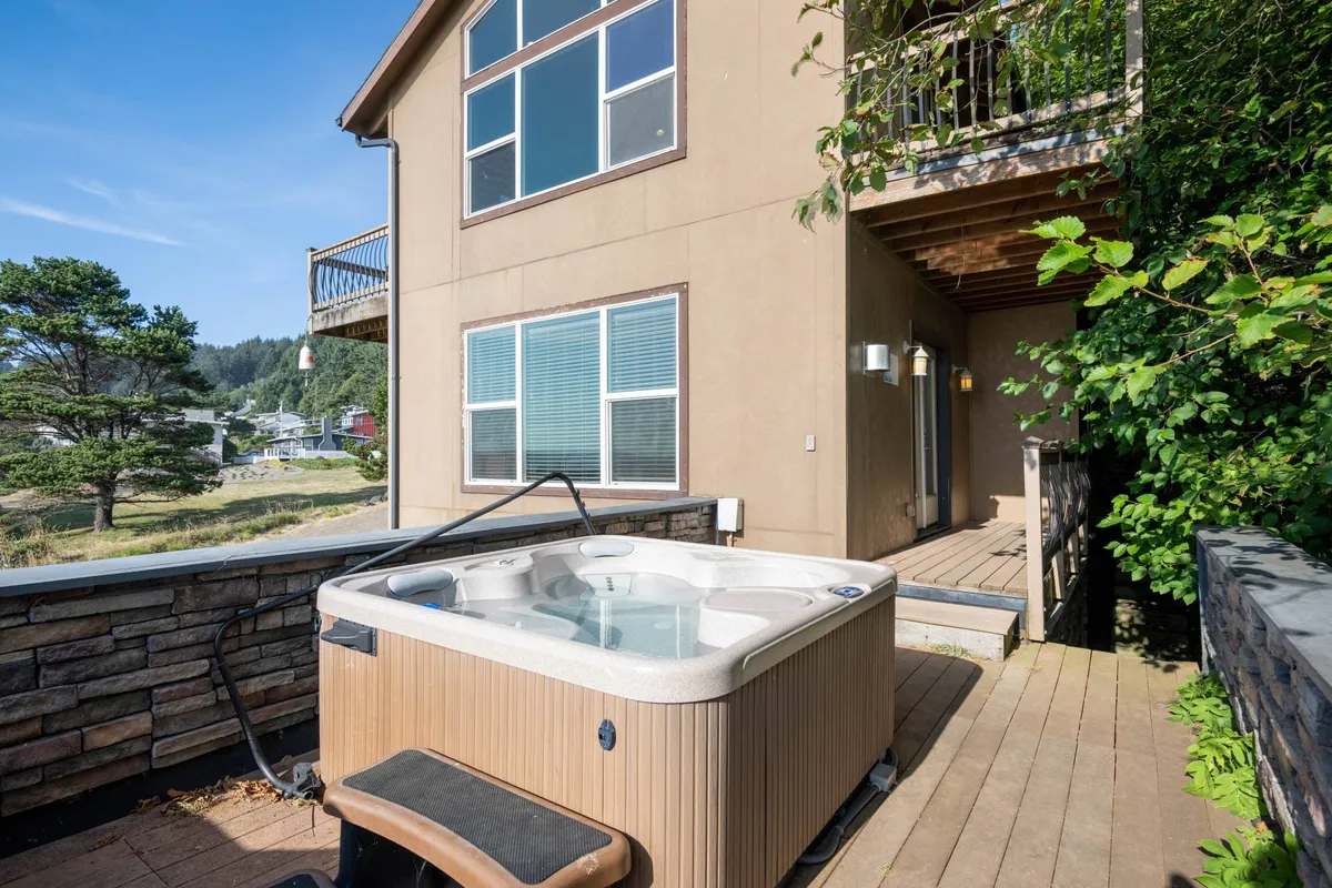 A serene deck area featuring a private hot tub surrounded by lush greenery. The hot tub is perfectly positioned for guests to unwind and soak while enjoying the tranquil outdoor setting, providing a sense of retreat after a day at the beach.