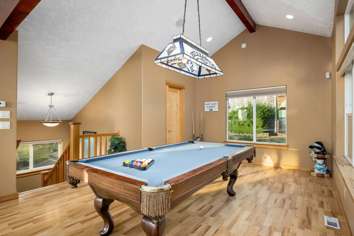 A bright, welcoming interior room featuring a pool table beneath a stained glass light fixture and a large window that lets in natural light. The setup is ideal for group activities and friendly competitions, complementing other indoor entertainment options.