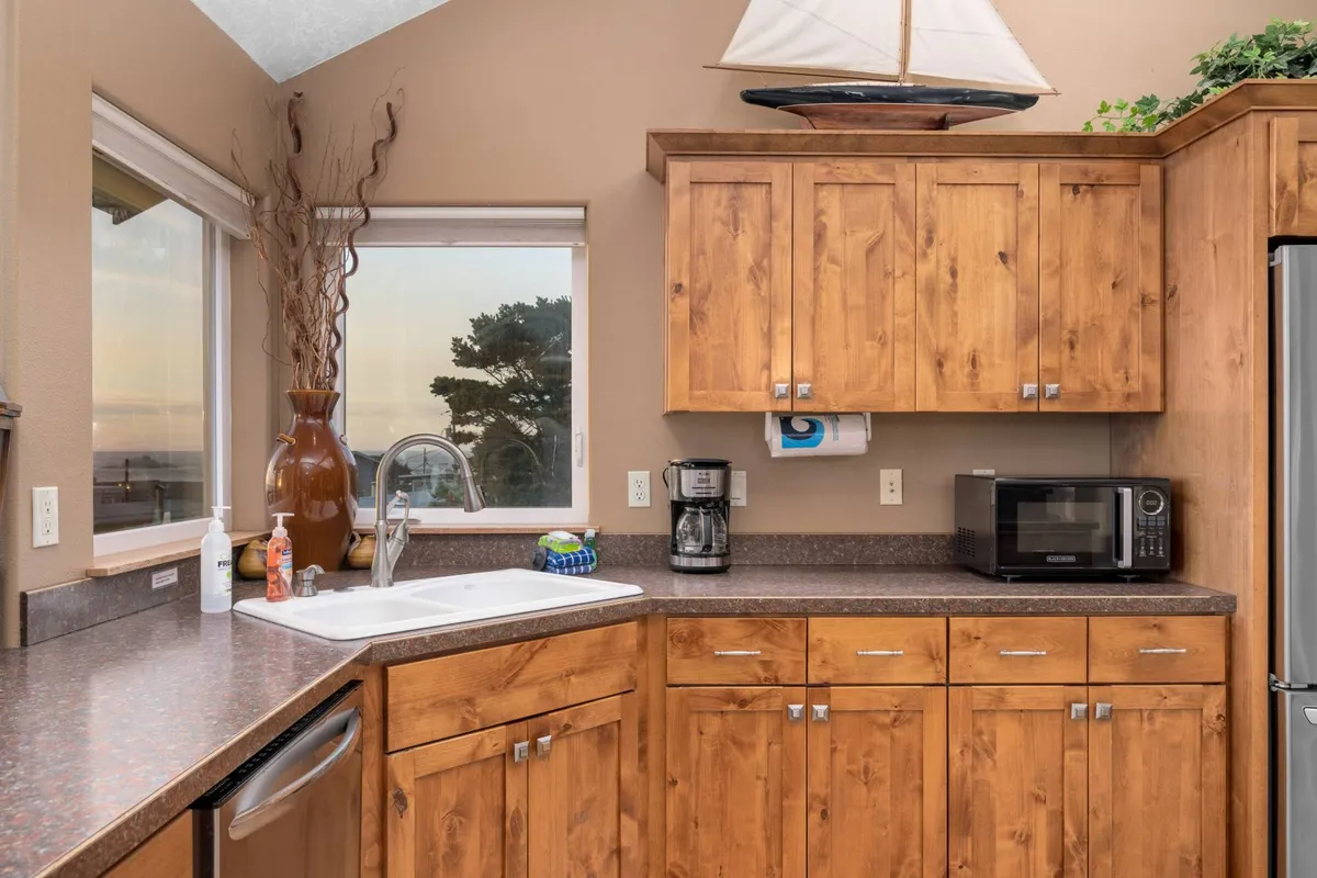 A compact kitchenette with wooden cabinets, a coffee maker, and microwave, accented by a window and nautical decor. The space feels cozy and efficient—ideal for preparing snacks or simple meals in a self-contained setting.