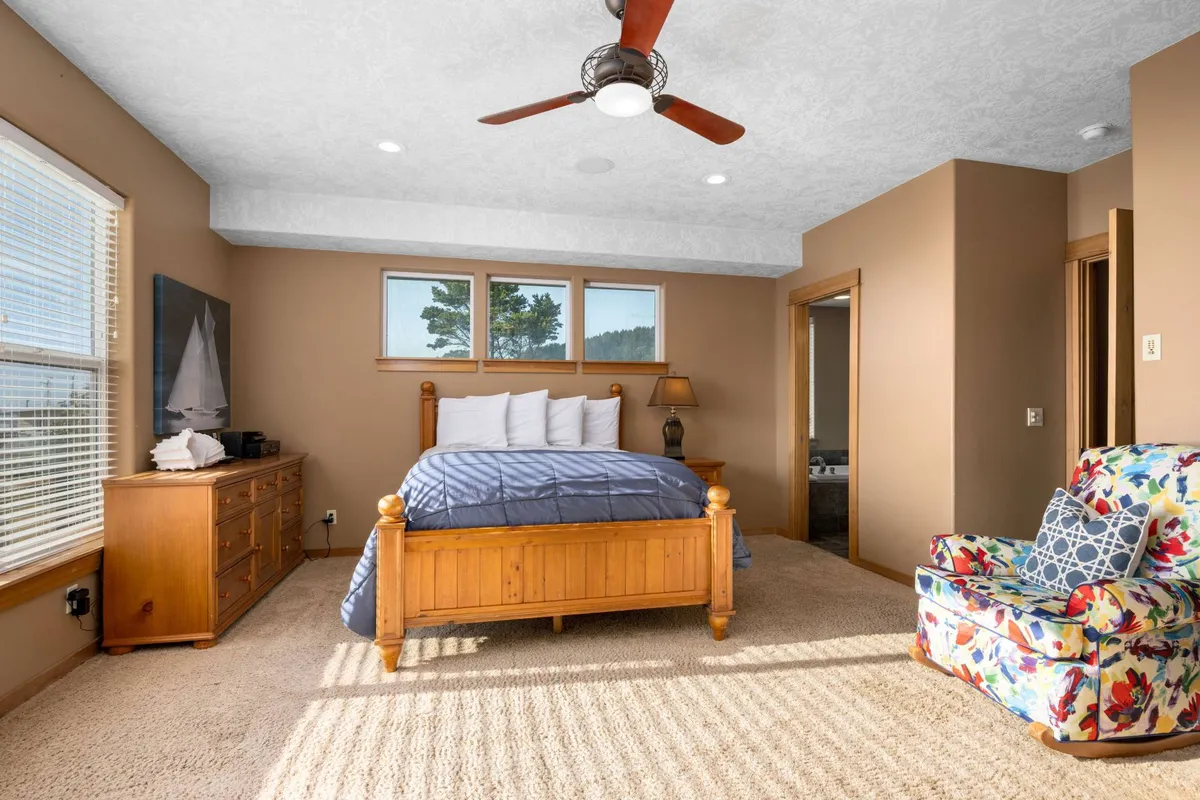 A light-filled bedroom with a wooden bed frame, colorful armchair, and expansive windows showcasing lush natural views. The space feels peaceful and calming, inviting guests to relax and enjoy a restful night.