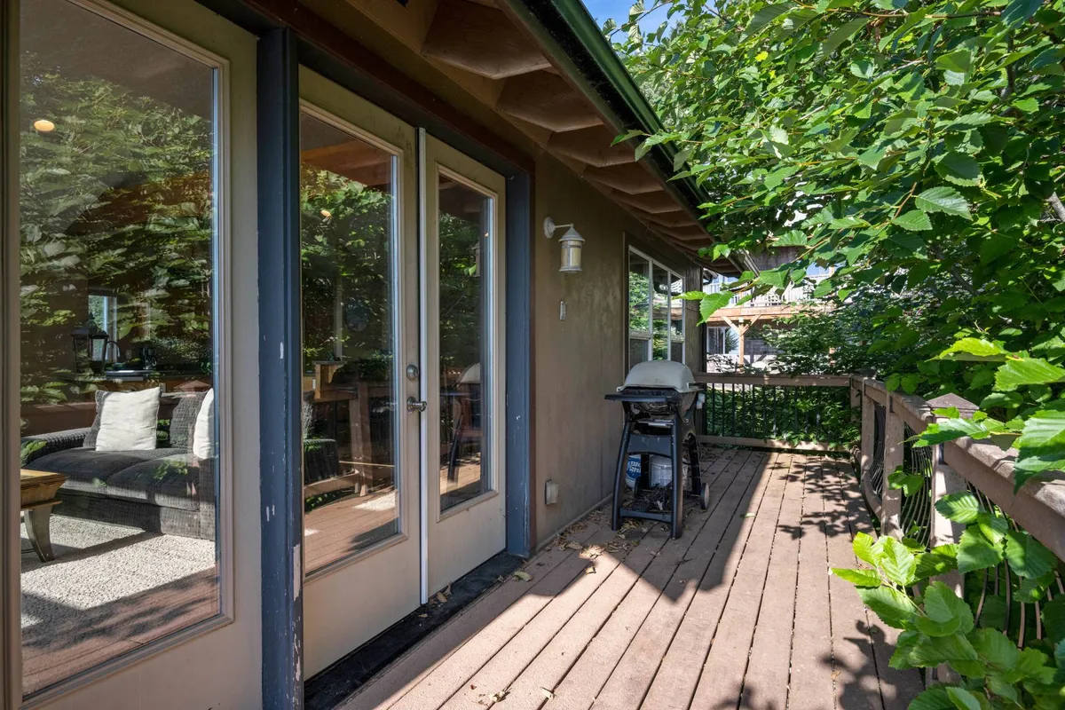 This exterior image showcases the spacious deck area with sliding glass doors leading into the home, a grill set up for barbecues, and ample room for outdoor dining and relaxing. The deck is surrounded by natural greenery, creating a peaceful and welcoming outdoor environment ideal for gatherings.